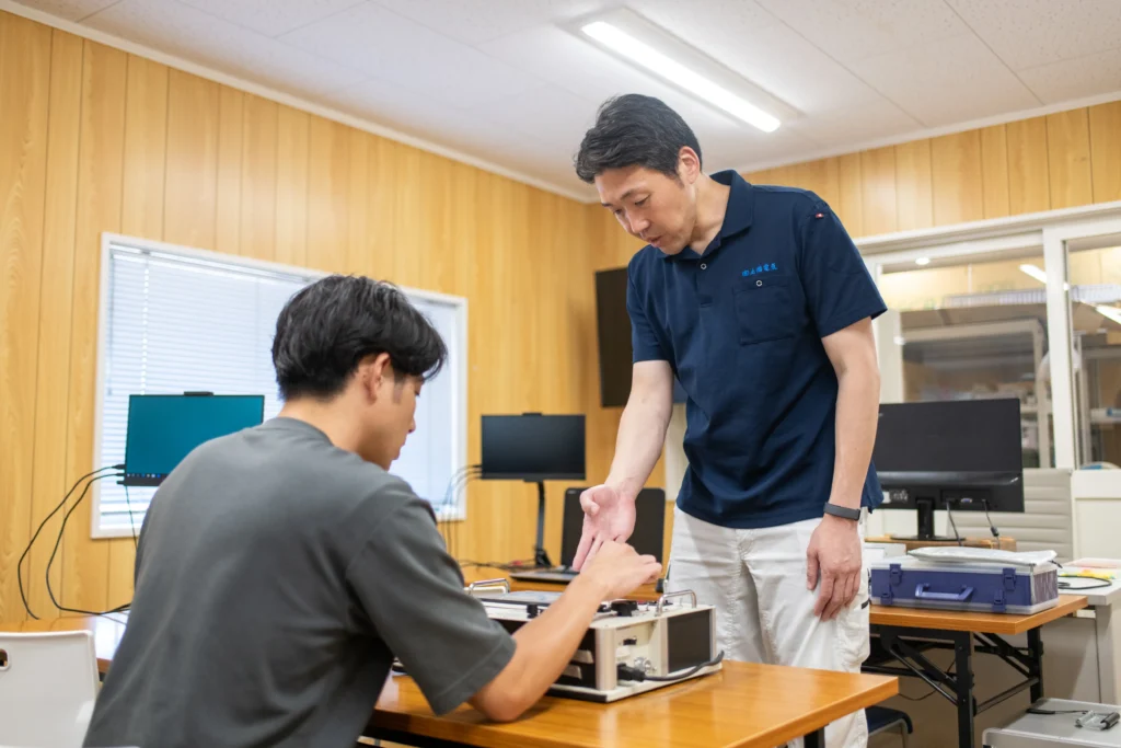 エンジニア研修にて熟練指導員が実技装置を操作する受講生に寄り添い実践的な技術ノウハウや機械制御のスキルを丁寧に教える