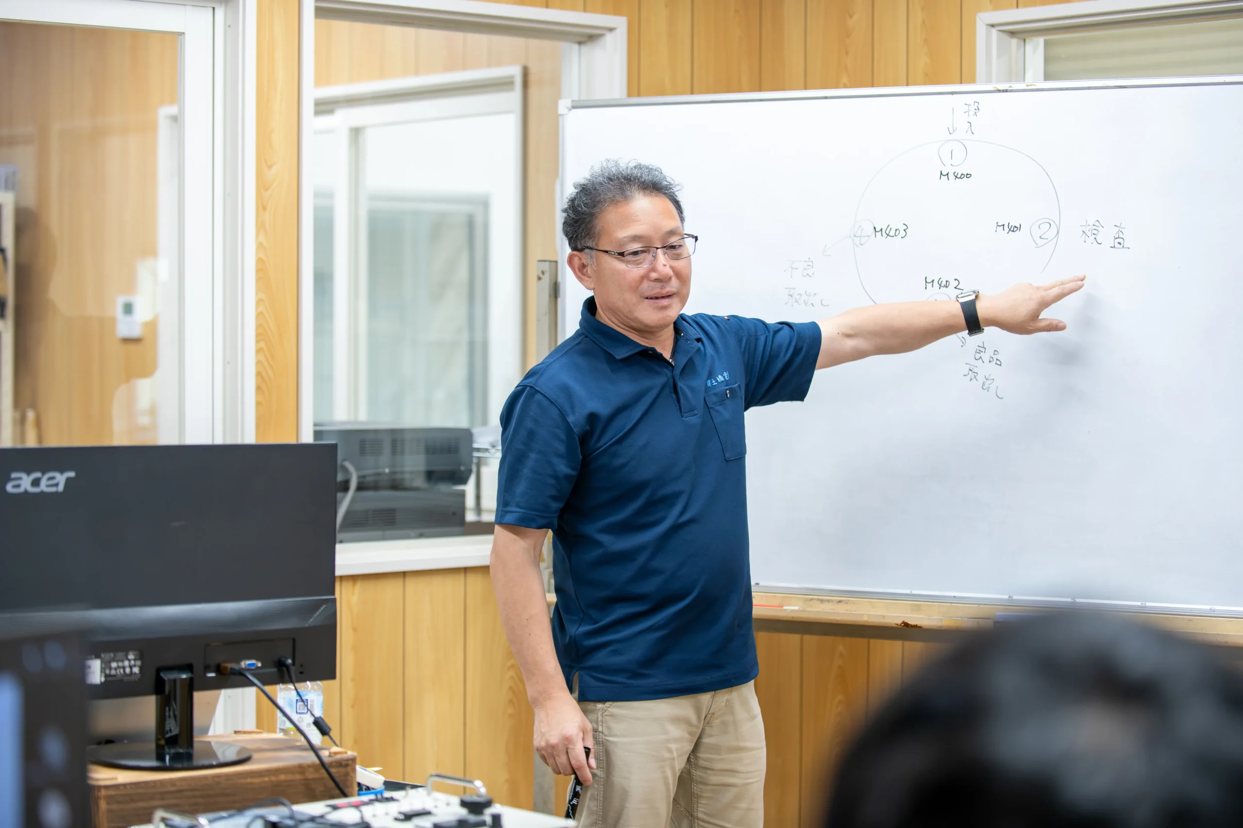 エンジニア育成研修で紺のシャツを着たベテラン講師がホワイトボードを使って実践的な技術指導を行う